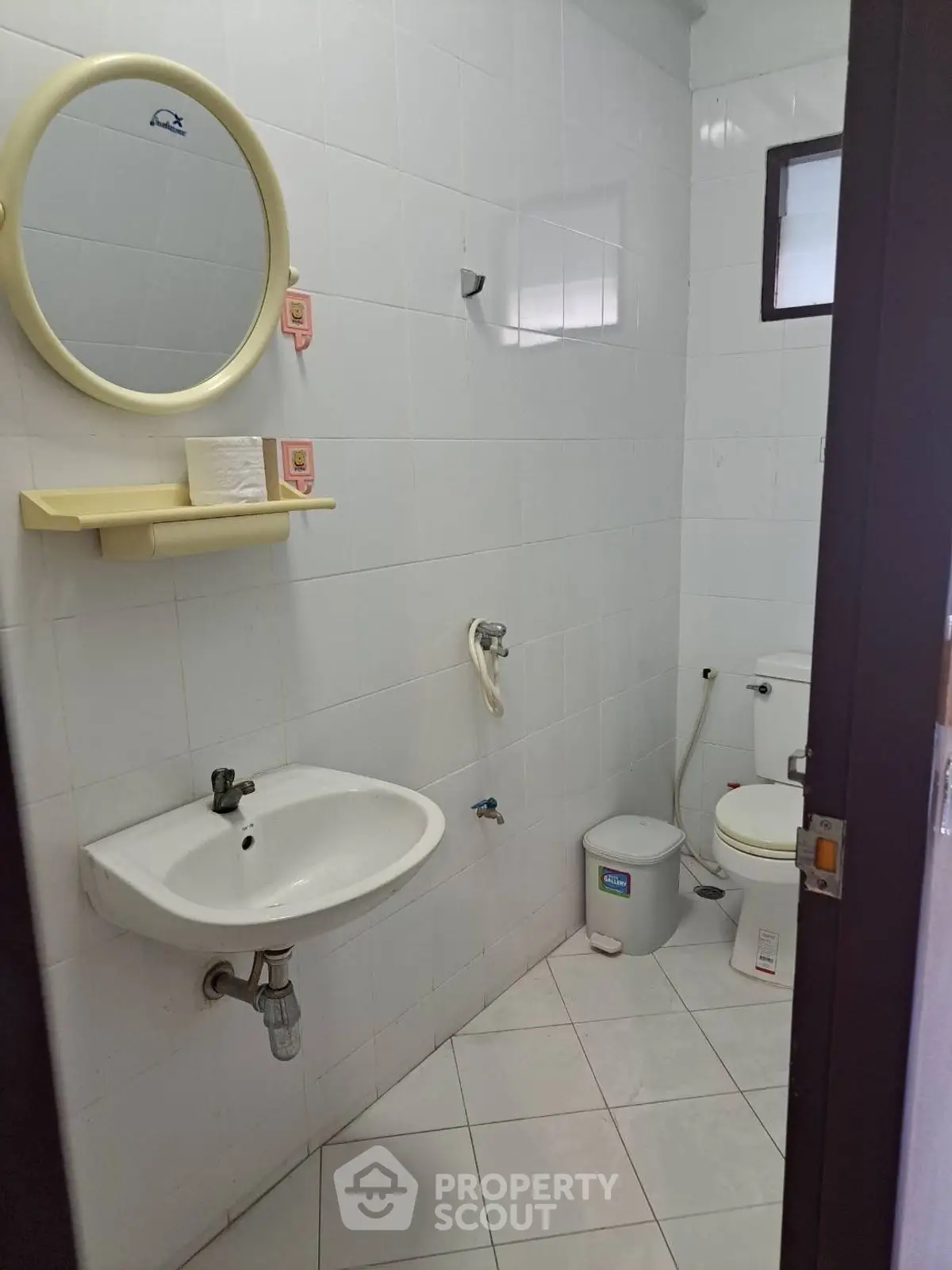 Compact bathroom with white tiles, round mirror, and basic fixtures.