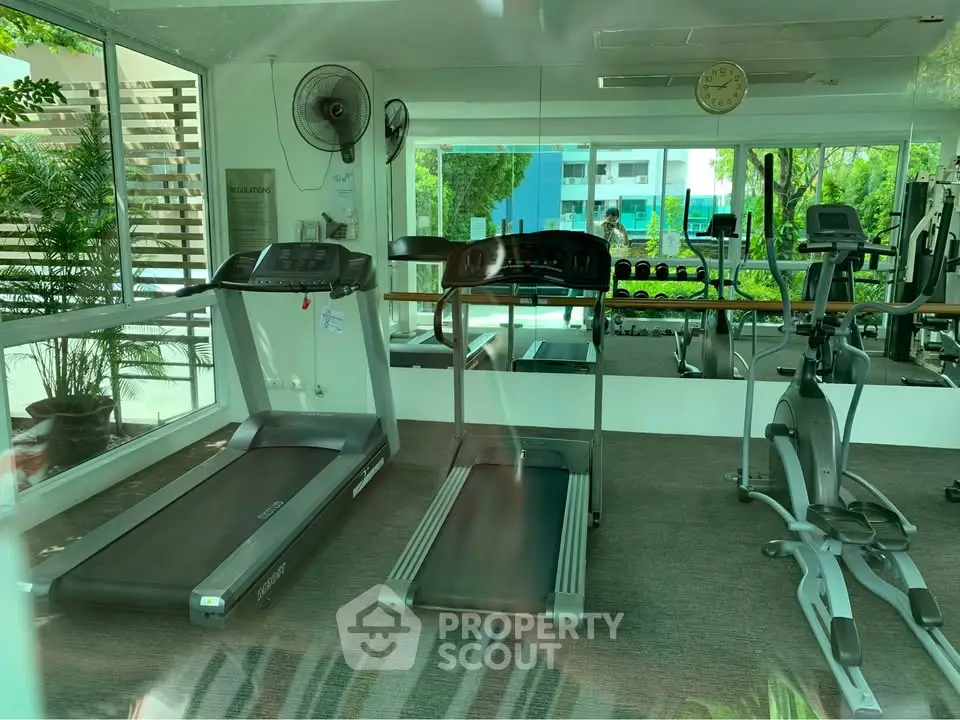 Modern gym with treadmills and exercise equipment in a bright, glass-walled space.
