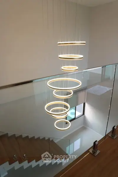 Modern staircase with elegant circular chandelier and glass railing