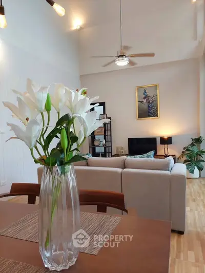 Spacious living room with high ceiling and elegant decor, featuring a cozy sofa and stylish lighting.