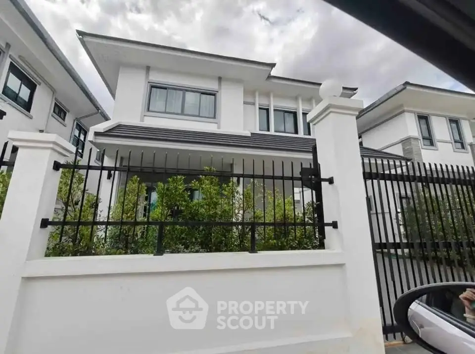 Modern two-story white house with black fence and lush greenery, showcasing contemporary architecture.