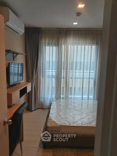 Cozy bedroom with natural light, featuring a bed, desk, and wall-mounted TV, ideal for modern living.