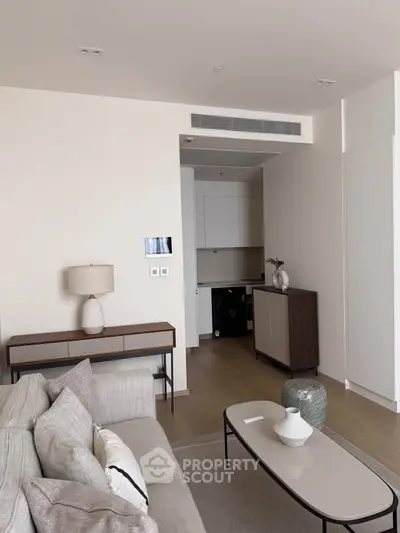 Modern living room with neutral tones, sleek furniture, and open layout leading to a compact kitchen area.