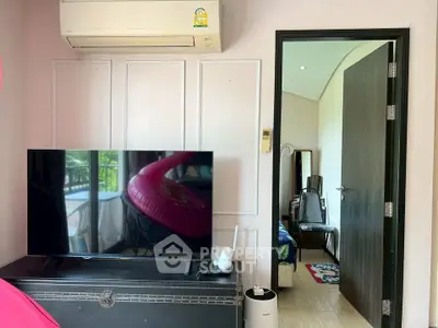 Modern living room with TV and air conditioning, leading to a cozy bedroom.