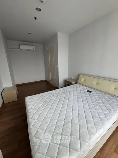 Spacious bedroom with modern design and wooden flooring, featuring a comfortable bed and air conditioning.