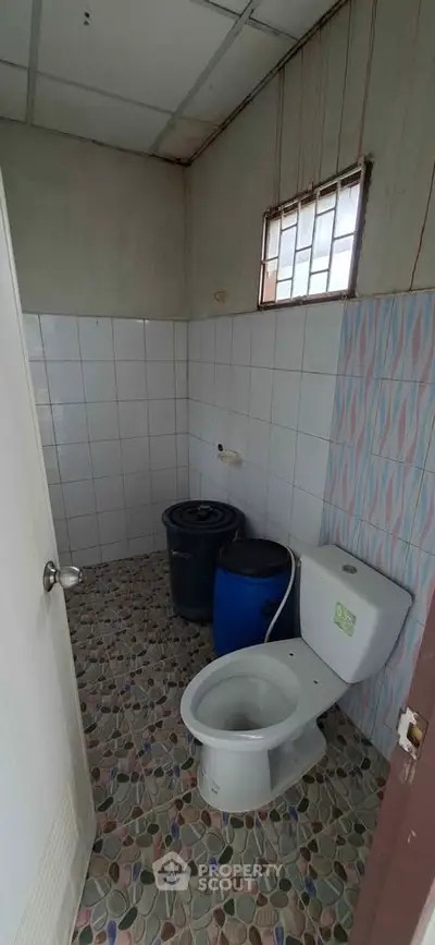 Compact bathroom with tiled walls and floor, featuring a toilet and water containers.