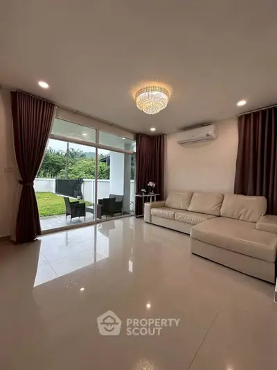 Spacious living room with modern decor and garden view, featuring elegant chandelier and comfortable seating.