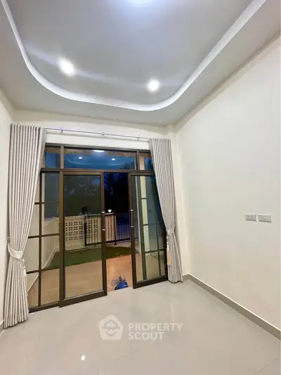 Spacious room with elegant ceiling and large glass doors leading to a balcony with serene views.