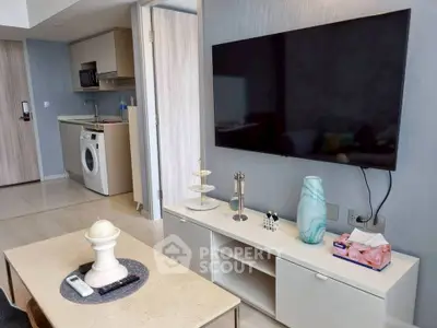 Modern living room with sleek TV setup and compact kitchen area in open layout apartment.