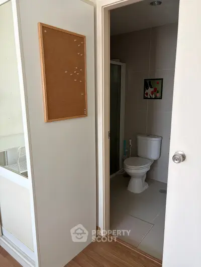 Compact bathroom with modern fixtures and a corkboard on the adjacent wall, showcasing efficient use of space.