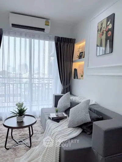 Modern living room with cozy gray sofa, elegant decor, and large window with city view.