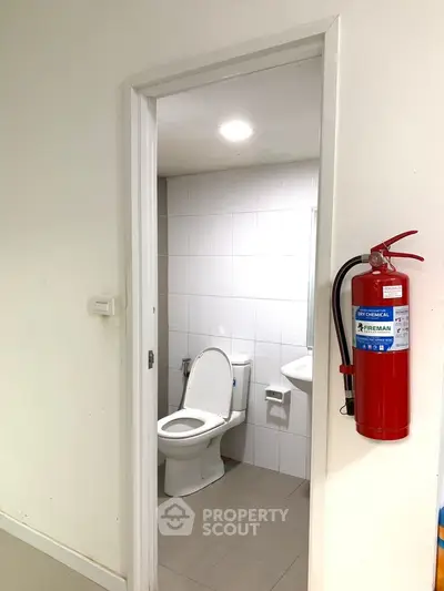 Compact bathroom with white tiles and fire extinguisher outside.