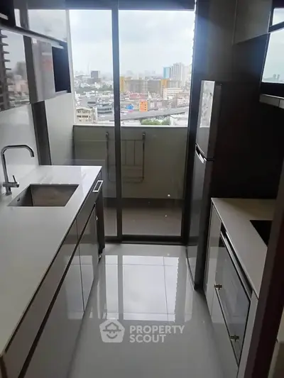 Modern kitchen with sleek design and city view from balcony, featuring built-in appliances and glossy white flooring.
