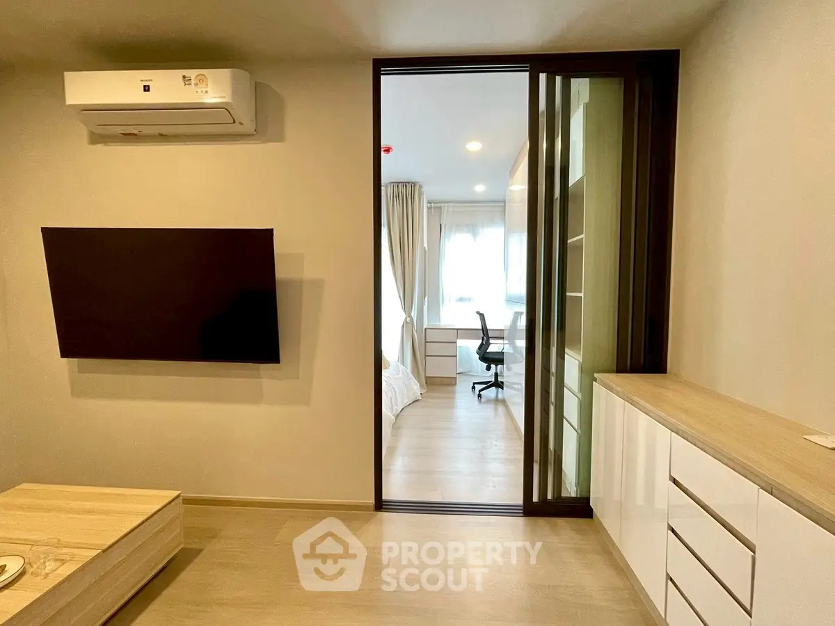 Modern living room with wall-mounted TV and view into a cozy bedroom