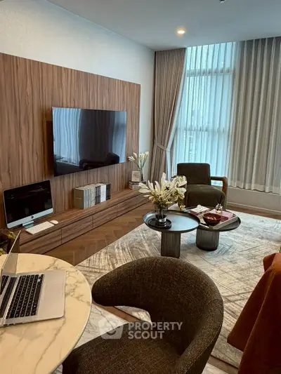 Modern living room with elegant decor, featuring a wall-mounted TV, stylish furniture, and large windows with curtains.