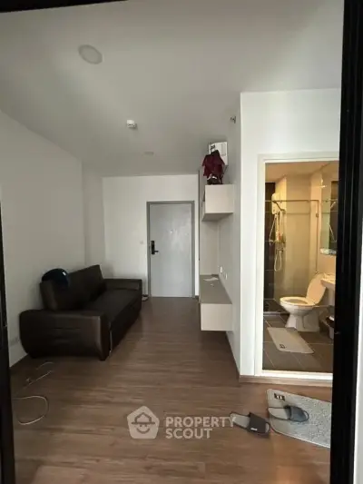Modern apartment interior with cozy living area and visible bathroom, featuring sleek wooden flooring.