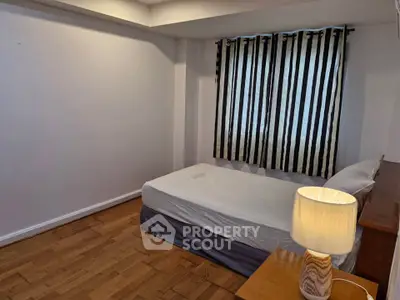 Cozy bedroom with wooden flooring and striped curtains, featuring a comfortable bed and a stylish lamp.