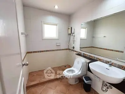 Modern bathroom with tiled floor, large mirror, and natural light from window.