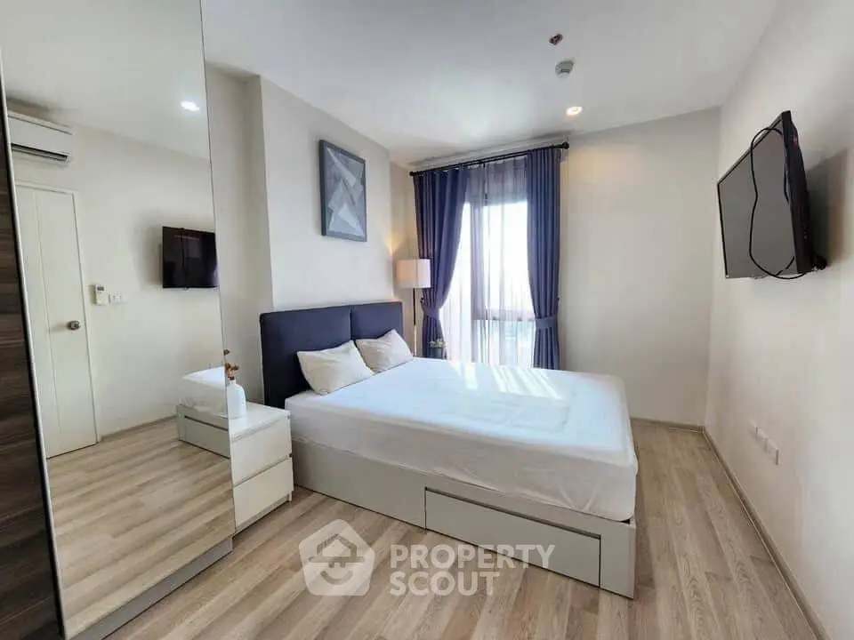 Modern bedroom with sleek design, featuring a large bed, wall-mounted TV, and natural light from a window.