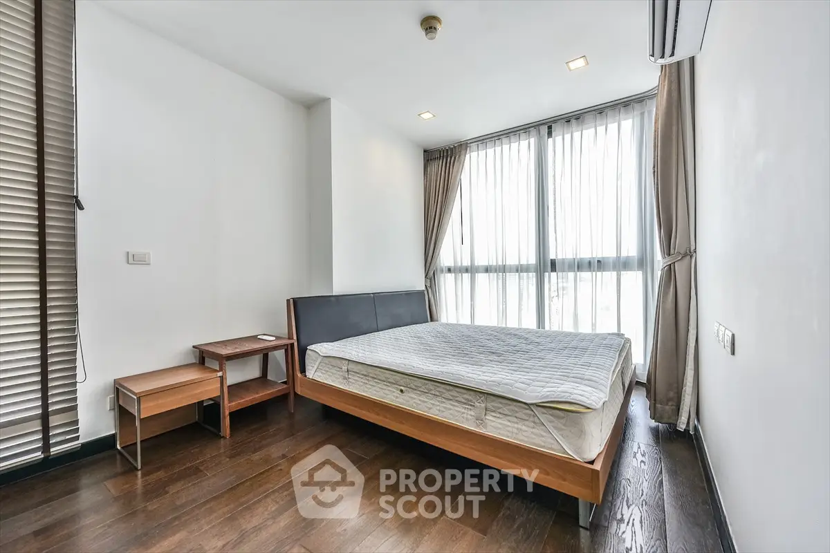 Spacious bedroom with large windows and modern wooden flooring in a stylish apartment.