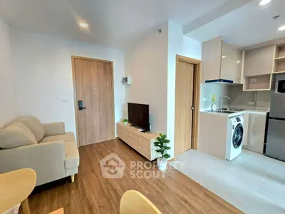 Modern open-plan living room with cozy sofa, TV, and compact kitchen featuring washing machine and fridge.