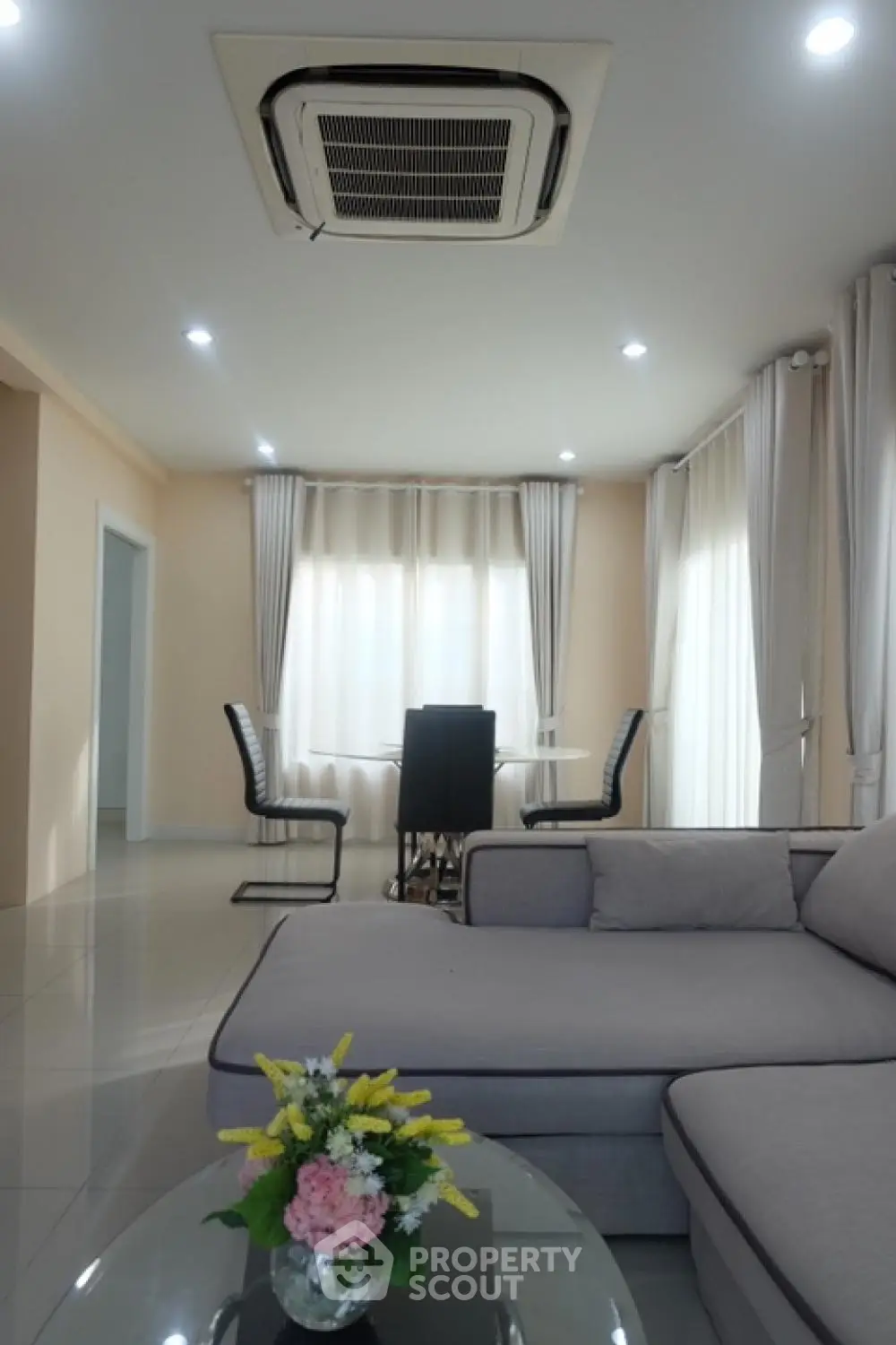 Spacious and modern living room with large sectional sofa, elegant dining area, and ample natural light filtering through sheer curtains, perfect for comfortable urban living.