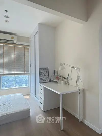 Modern bedroom with study area, featuring a sleek desk and city view from large window.