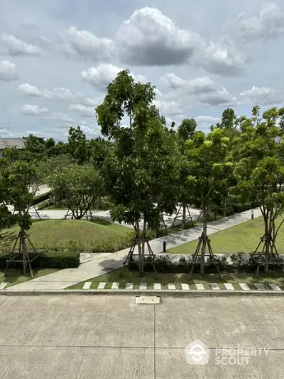 Lush green garden view with paved pathways and trees under a cloudy sky.