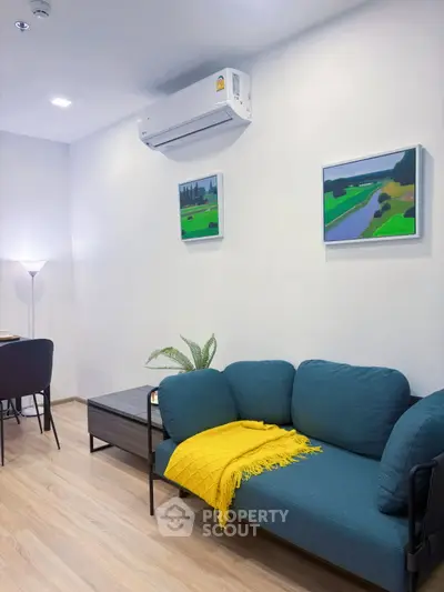 Modern living room with teal sofa, yellow throw, and wall art, featuring sleek air conditioning unit.