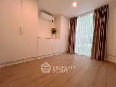 Spacious bedroom with wooden flooring and large window for natural light.