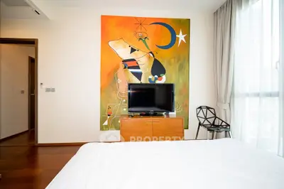 Modern bedroom with abstract art, TV, and stylish chair, featuring large window with natural light.
