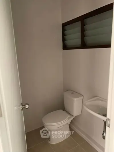 Compact bathroom with modern toilet and small sink, featuring frosted glass window for privacy.