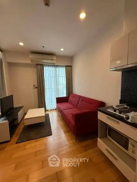 Modern living room with red sofa, wooden flooring, and compact kitchen area in a cozy apartment.