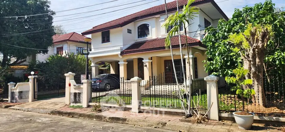 Charming two-story house with red roof, lush garden, and gated entrance in a serene neighborhood.