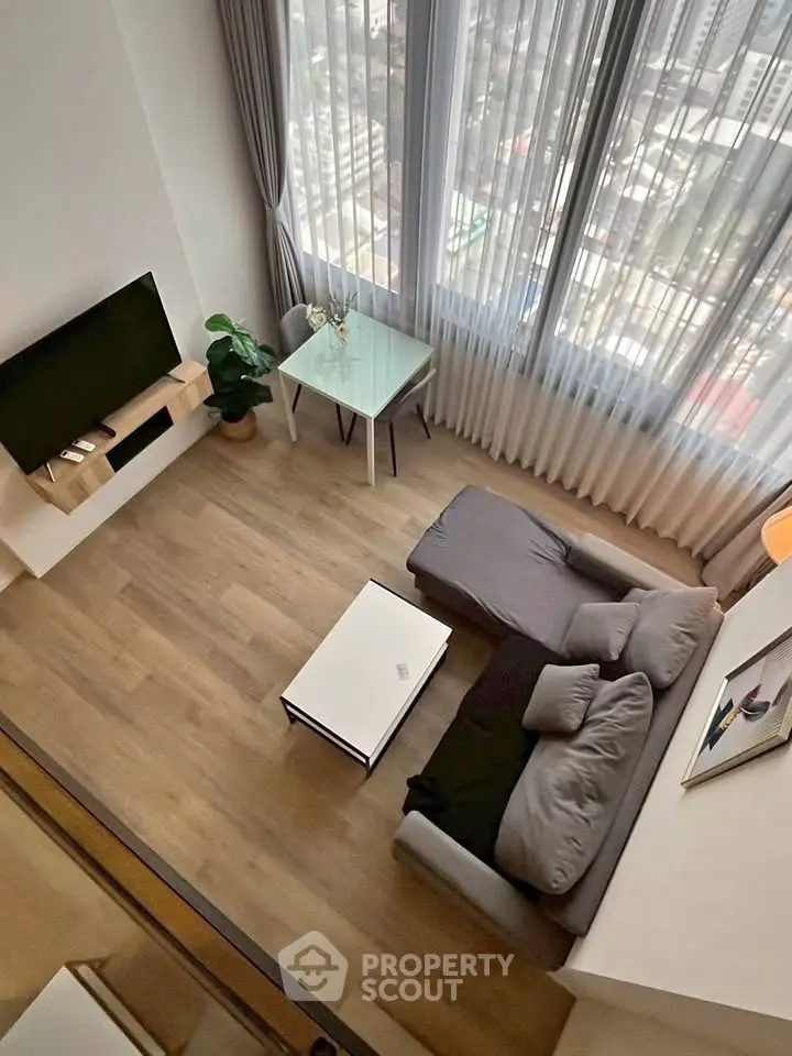 Modern living room with high ceiling and city view, featuring sleek furniture and large windows.