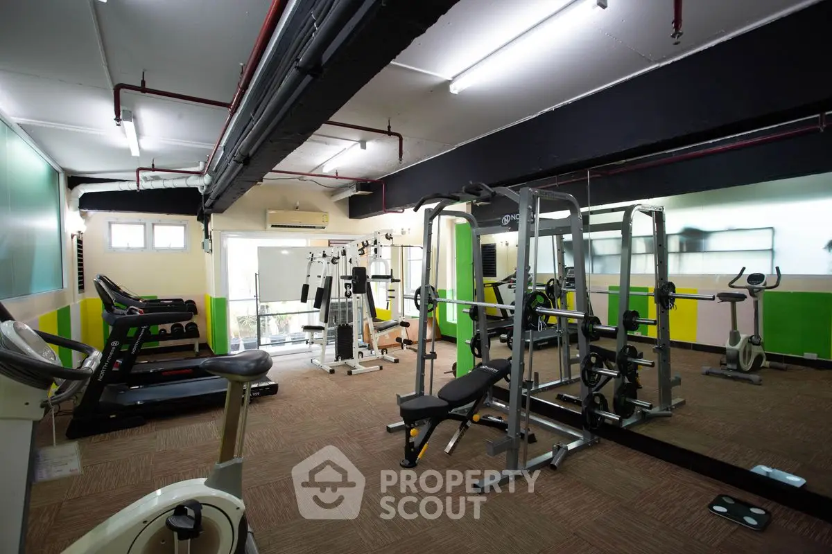 Spacious gym with modern fitness equipment and mirrored walls in a residential building.