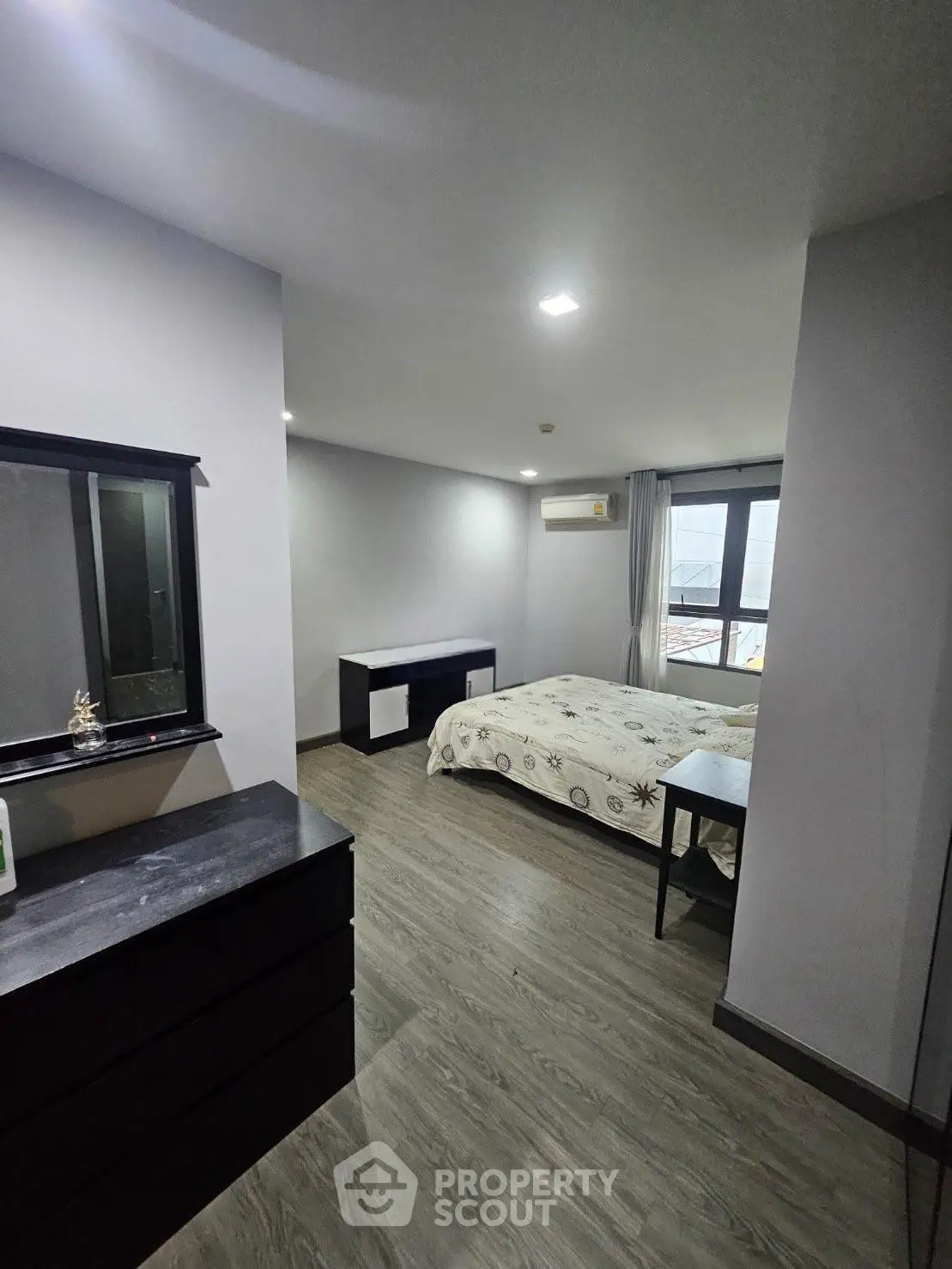 Spacious bedroom with modern decor and large window offering natural light.