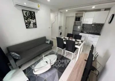 Modern living room with open kitchen, featuring sleek furniture and appliances.