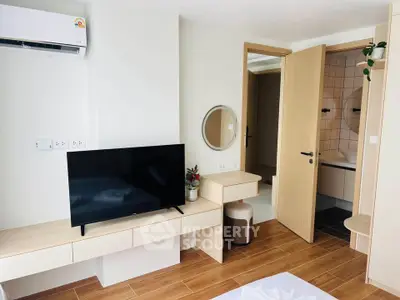 Modern bedroom with TV and ensuite bathroom, featuring sleek wooden flooring and minimalist decor.
