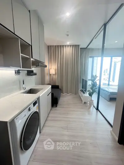 Modern apartment with sleek kitchen and cozy living area, featuring glass partition and stylish decor.