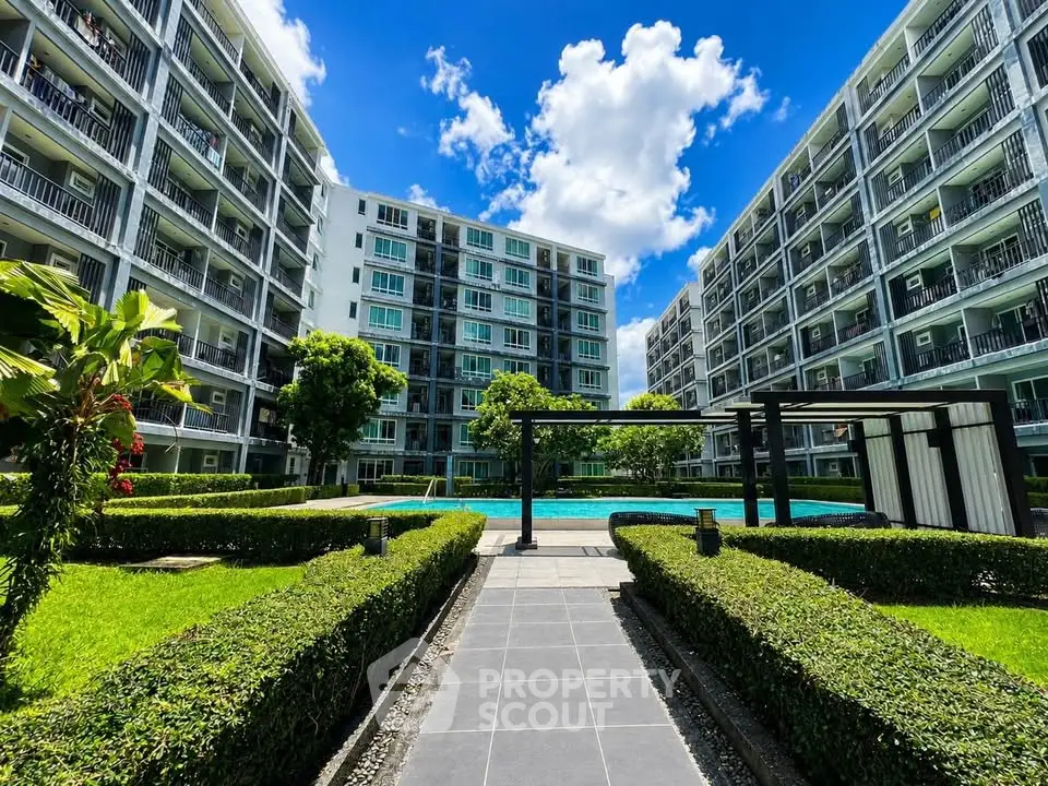 Modern apartment complex with lush gardens and a central pool under a bright blue sky.