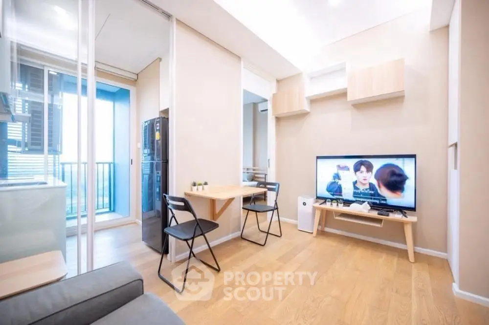 Modern living room with TV and balcony view, featuring sleek furniture and wooden flooring.
