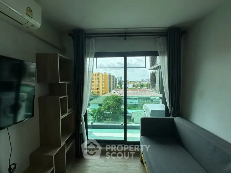 Modern living room with large window and city view, featuring sleek furniture and natural light.