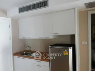 Compact kitchen with white cabinets and stainless steel fridge in modern apartment