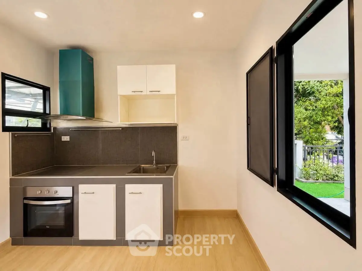 Modern kitchen with sleek design, featuring built-in oven and large windows overlooking lush greenery.