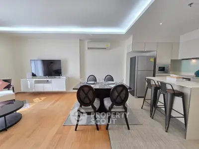 Spacious modern living room with dining area and open kitchen, featuring sleek furniture and wooden flooring.