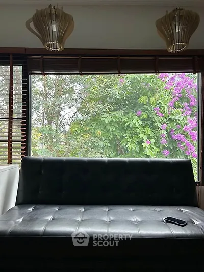 Cozy living room with large window and garden view, featuring modern lighting and sleek black sofa.
