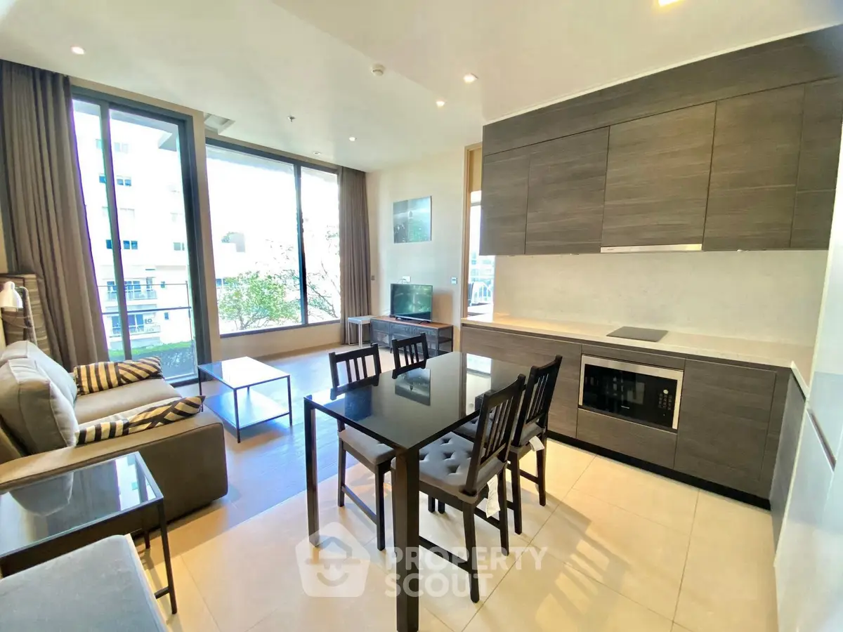 Modern open-layout living room with kitchen, featuring sleek cabinetry and large windows for natural light.