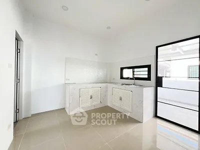 Modern minimalist kitchen with sleek white cabinetry and large window for natural light.