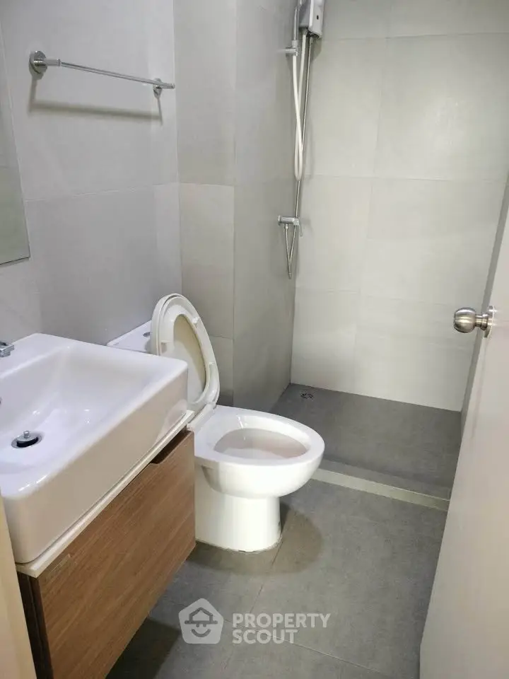 Modern bathroom with sleek fixtures and minimalist design, featuring a shower and compact sink.